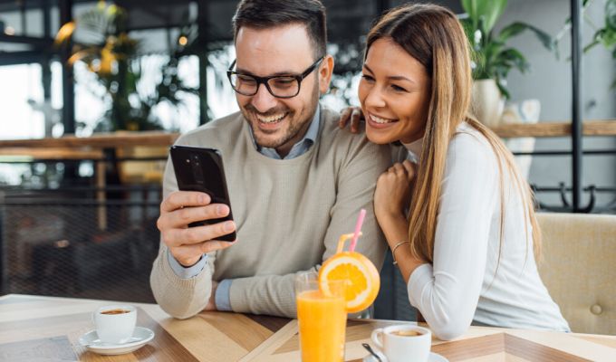 Uśmiechnięta para w restauracji patrzy na telefon