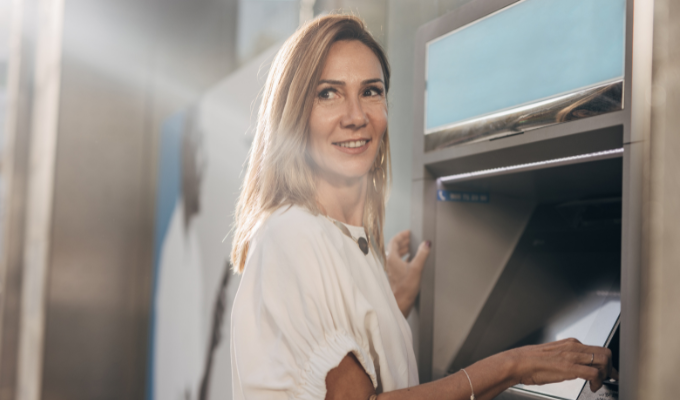 Kobieta przed bankomatem trzymająca w ręku kartę